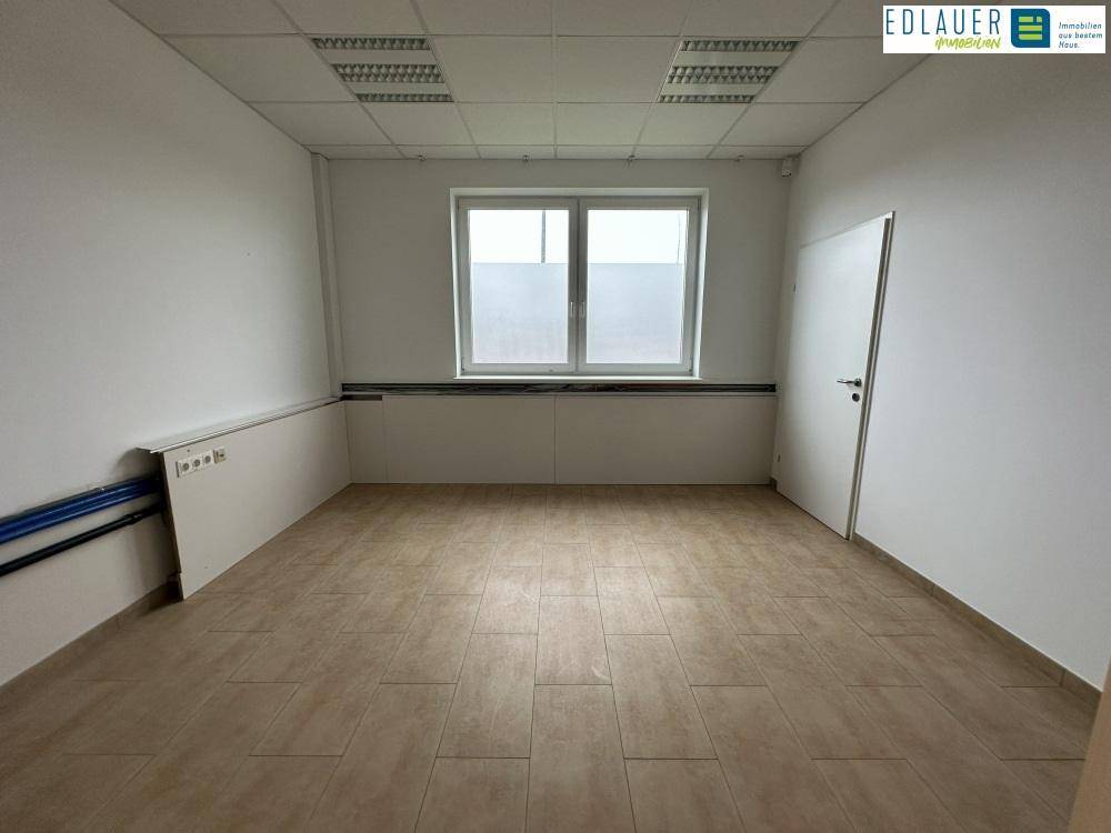 Heller Büroraum mit Fliesenboden, Fenster und weißer Tür, bereit für individuelle Einrichtung und Nutzung.