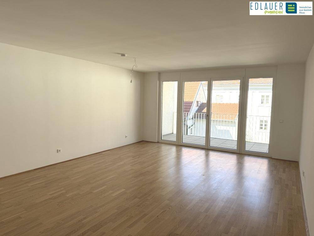 Lichtdurchflutetes Wohnzimmer mit Parkettboden und breiter Fensterfront zum Balkon.