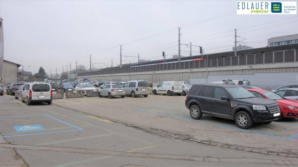 Weitläufiger Parkplatz neben Bahngleisen mit verschiedenen Fahrzeugen.