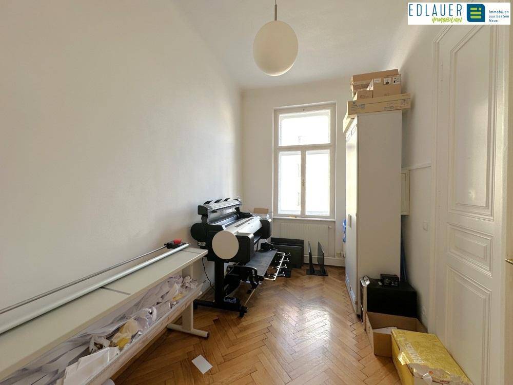 Funktionaler Raum mit Holzboden, Fenster und einem Großformatdrucker, genutzt als Arbeits- oder Lagerbereich.