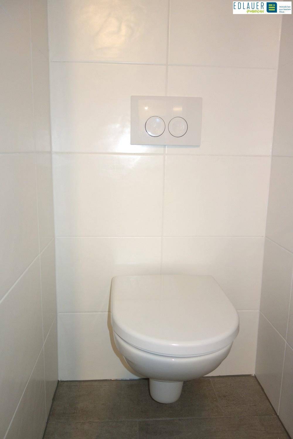 Separates WC mit wandhängender Toilette und weißen Fliesen an den Wänden.