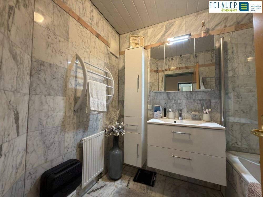 Elegantes Badezimmer mit Marmorwänden, Waschtisch und beheiztem Handtuchhalter.