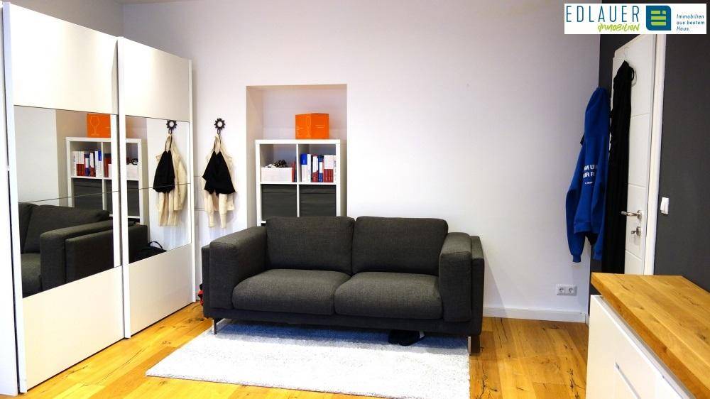 Wohnbereich mit dunklem Sofa, Spiegelschrank und Holzboden.