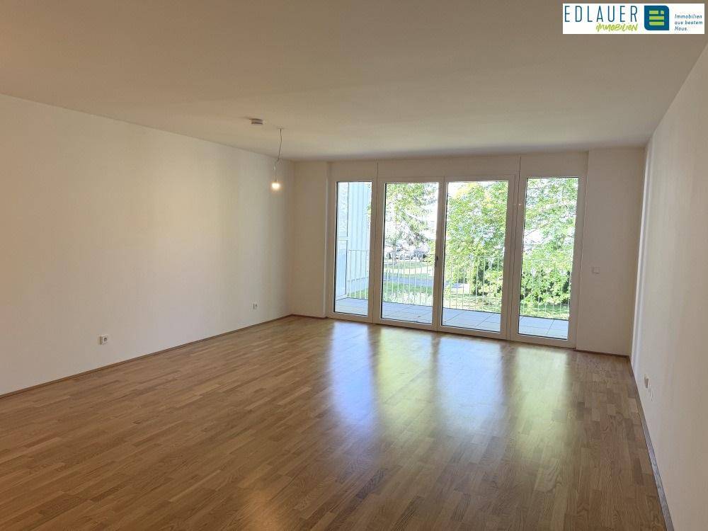Helles Wohnzimmer mit Parkettboden und großen Fenstern, die Zugang zu einem Balkon bieten.