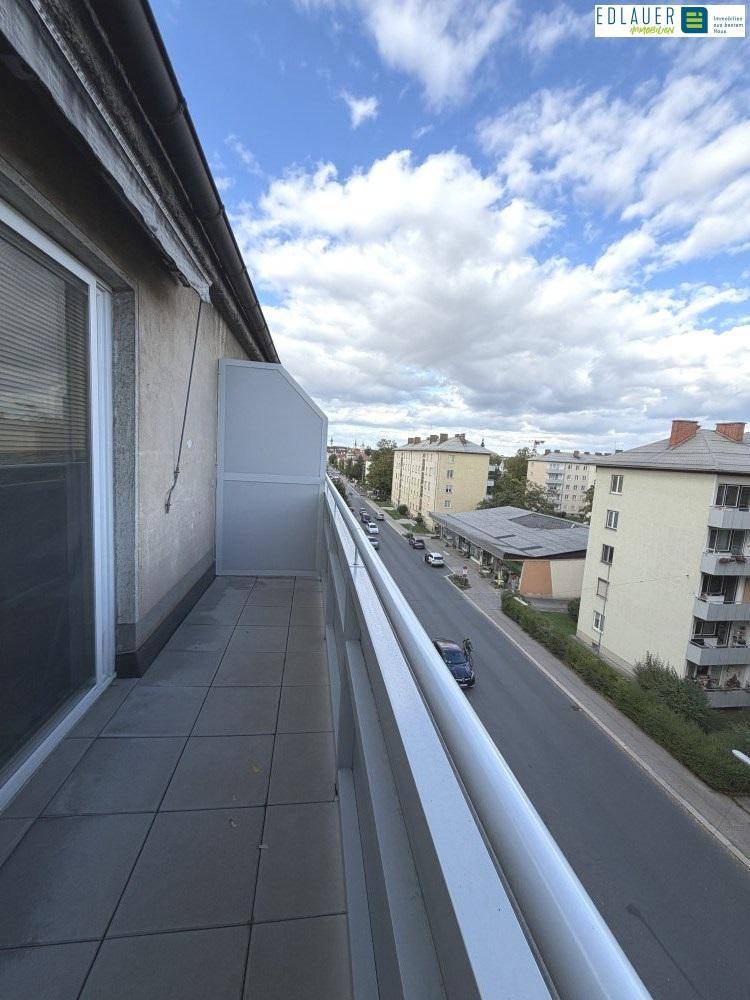 Langer Balkon mit Fliesenboden und Blick auf die Straße und umliegende Gebäude.