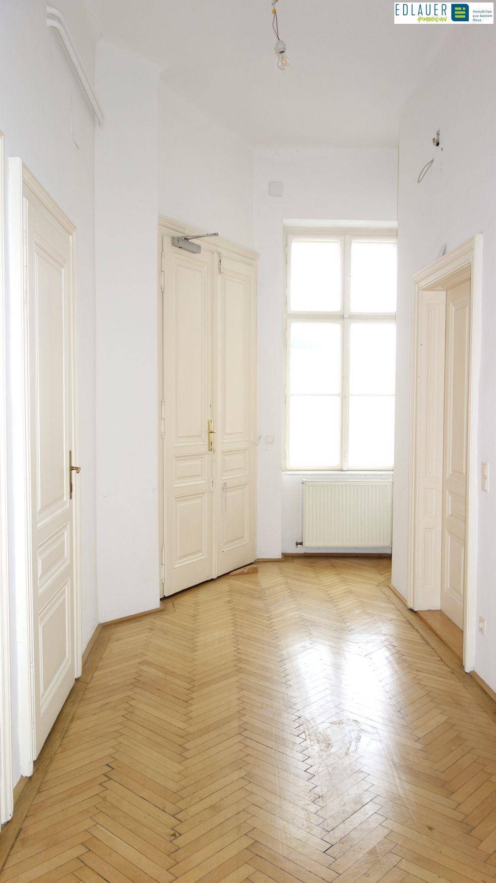 Breiter Flur mit Fischgrätparkett, hohen Türen und einem Fenster, das natürliches Licht hereinlässt.