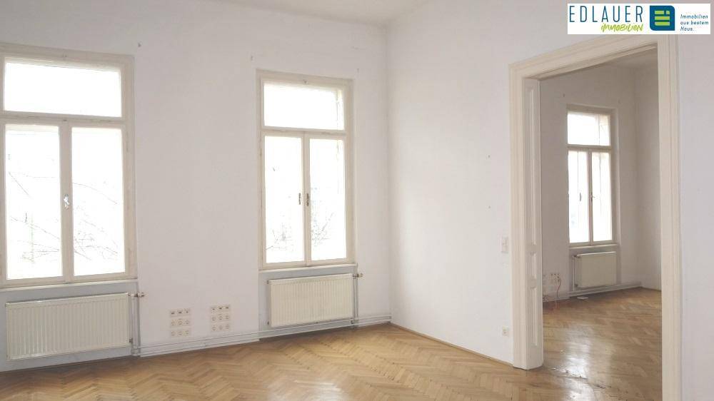 Großer, heller Raum mit klassischem Fischgrätparkett und zwei hohen Fenstern, ideal für Wohnzwecke.