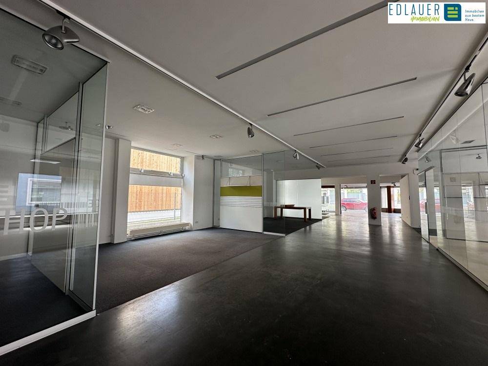 Großer, offener Bürobereich mit Teppichboden, Glaswänden und Blick auf die Straße, ideal für moderne Arbeitskonzepte.