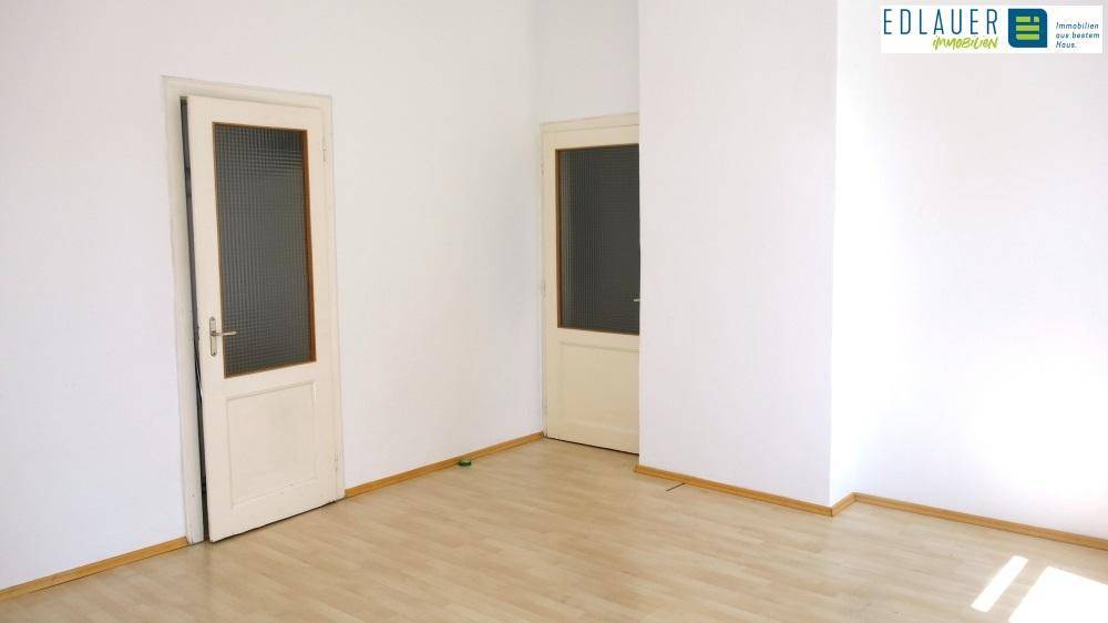 Leerer Raum mit zwei Türen und hellem Laminatboden, der auf weitere Bereiche führt.