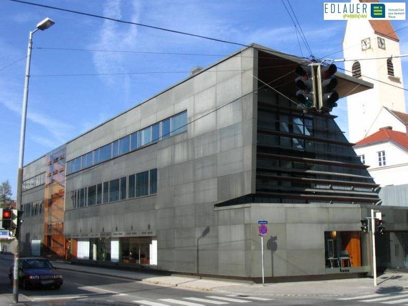Modernes Geschäftsgebäude mit Betonfassade und großen Fenstern an einer städtischen Kreuzung.