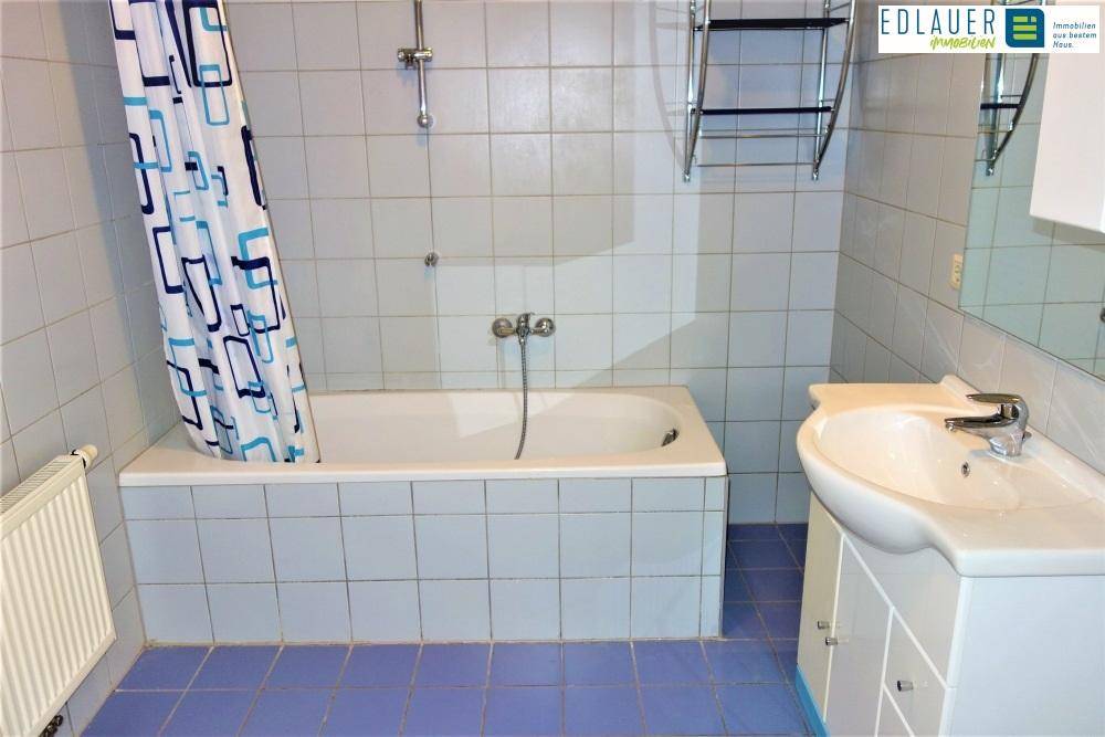 Badezimmer mit Badewanne, Waschbecken und hellblauen Fliesen an Wänden und Boden.