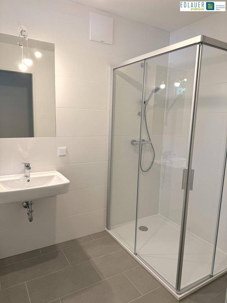 Modernes Badezimmer mit geräumiger Duschkabine, Waschbecken und Spiegel.