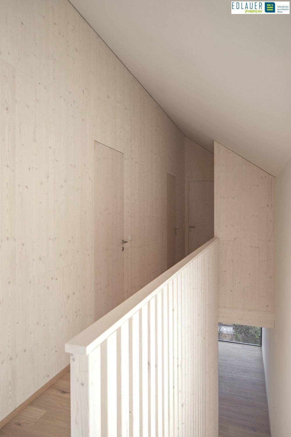 Heller Flur im Obergeschoss mit Holzwänden und schrägen Decken, die ein Gefühl von Weite vermitteln.