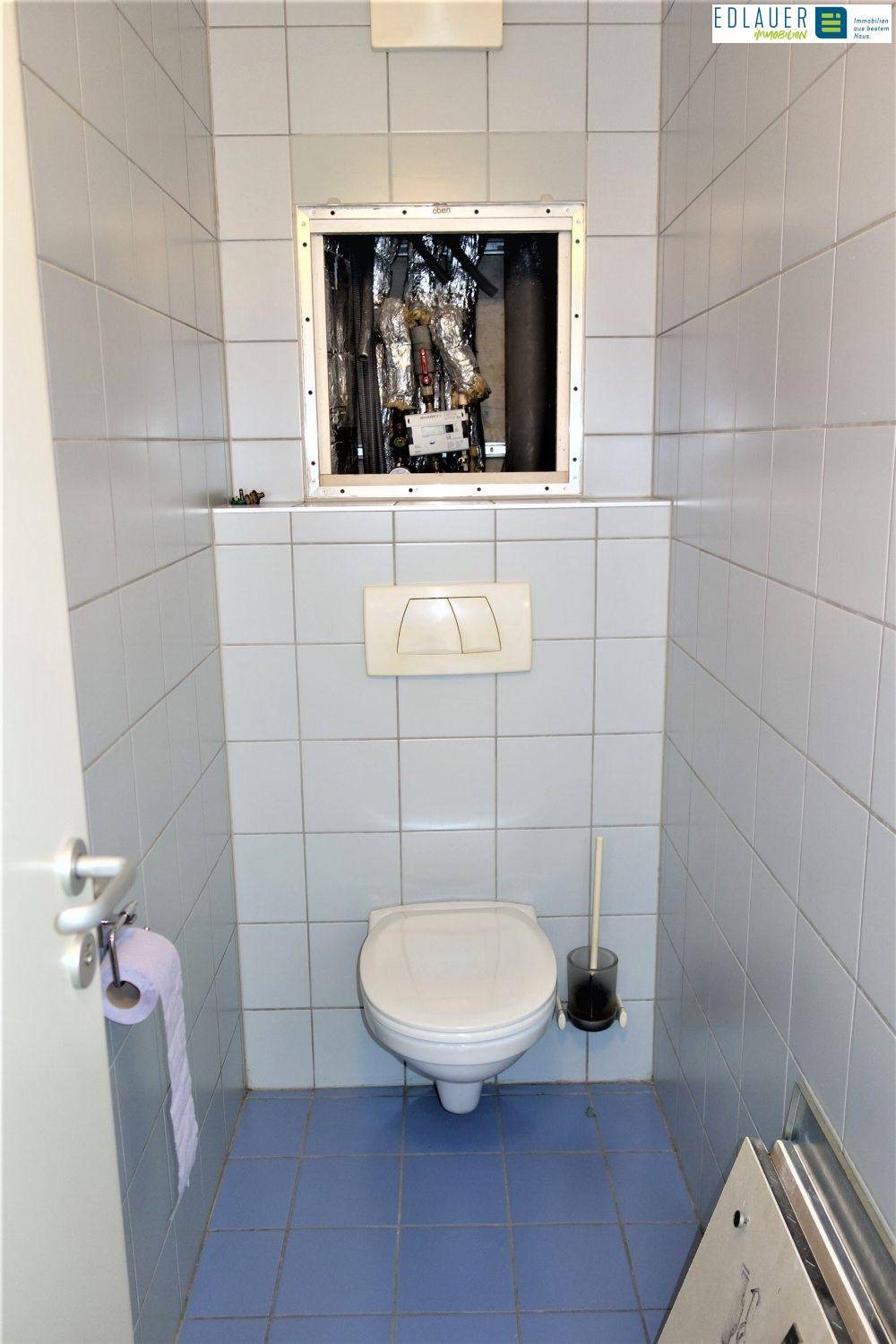 Separate Toilette mit hellblauen Fliesen und einem Spülkasten mit Revisionsklappe.