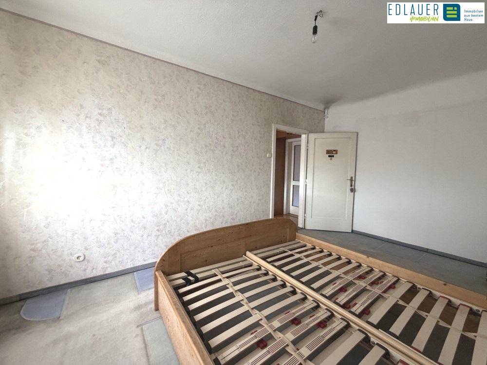 Helles Schlafzimmer mit Teppichboden und strukturierten Tapeten, bietet Potenzial zur Modernisierung.