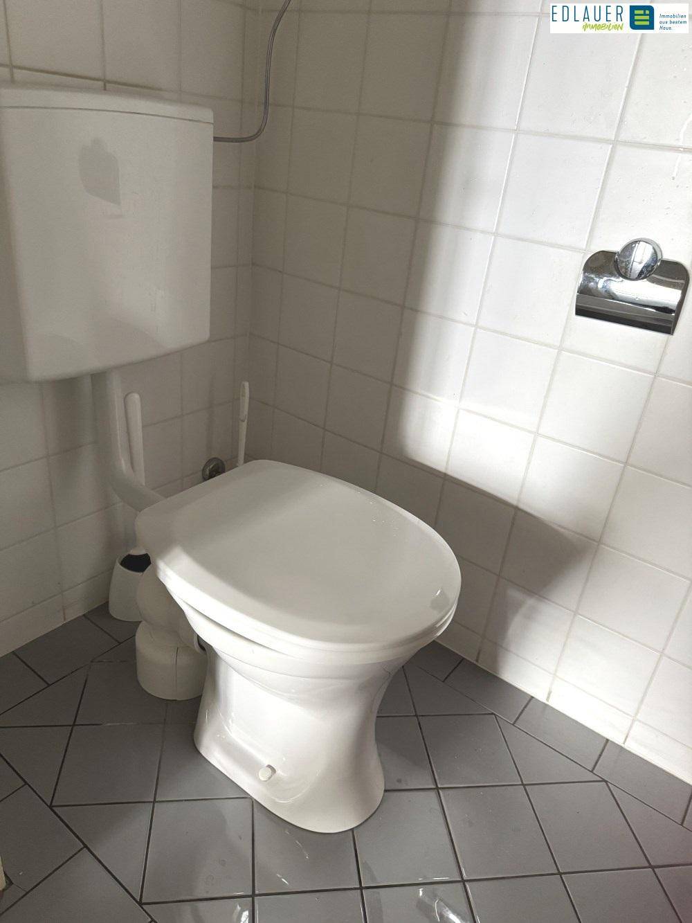 Toilette mit weißen Wandfliesen und grauen Bodenfliesen, ausgestattet mit einem modernen WC.