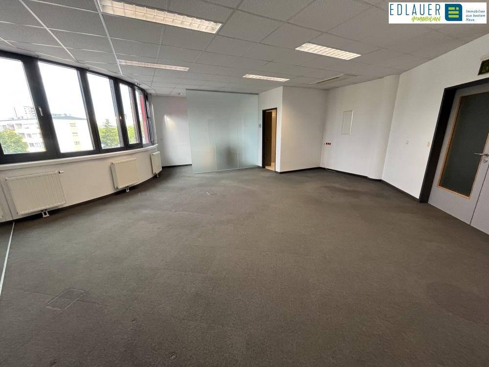 Weitläufiger Bürobereich mit Teppichboden, großen Fenstern und Heizkörpern, bietet viel Tageslicht.
