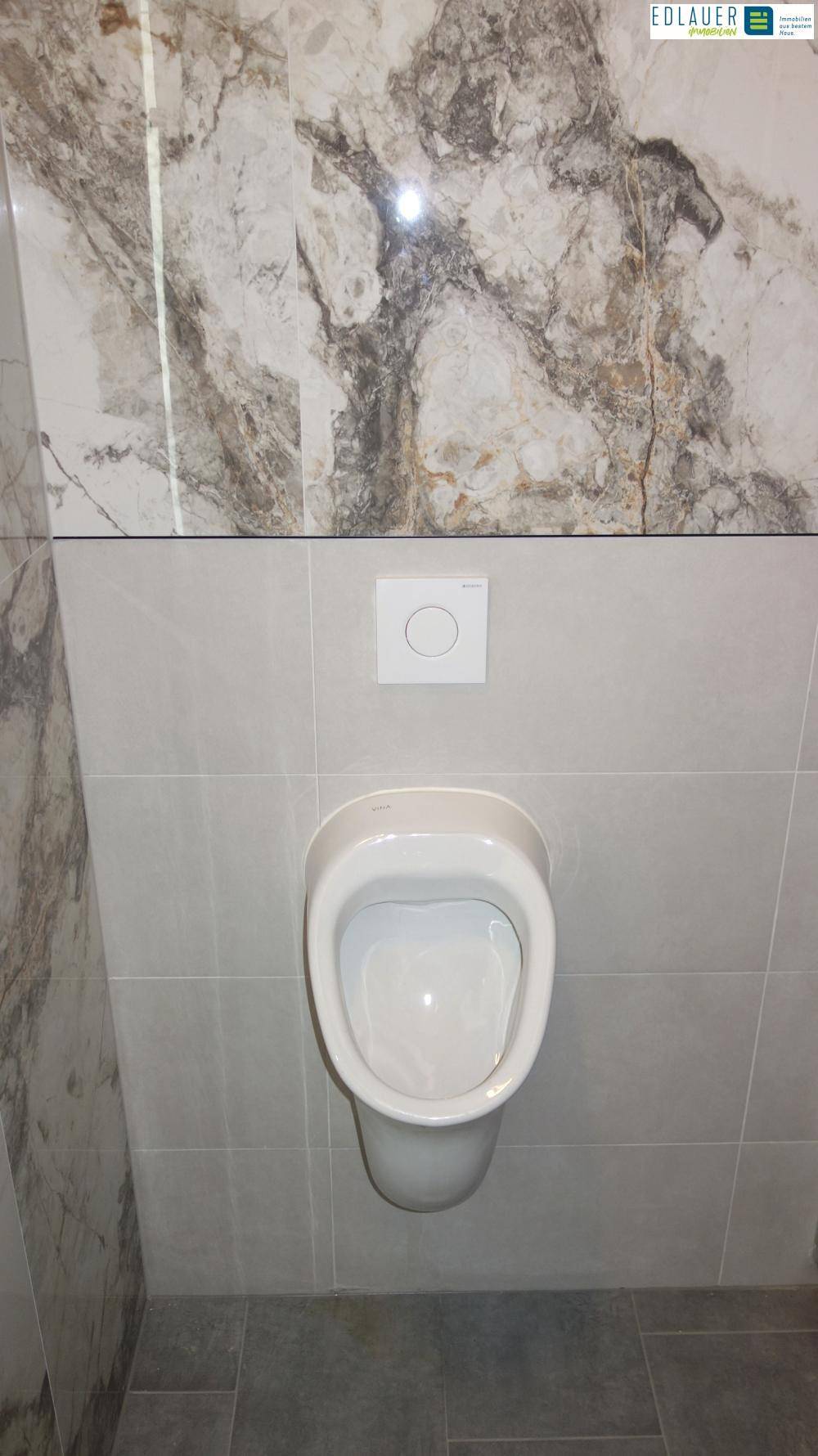 Modernes Badezimmer mit Urinal und Fliesen in Marmor-Optik und Grau.
