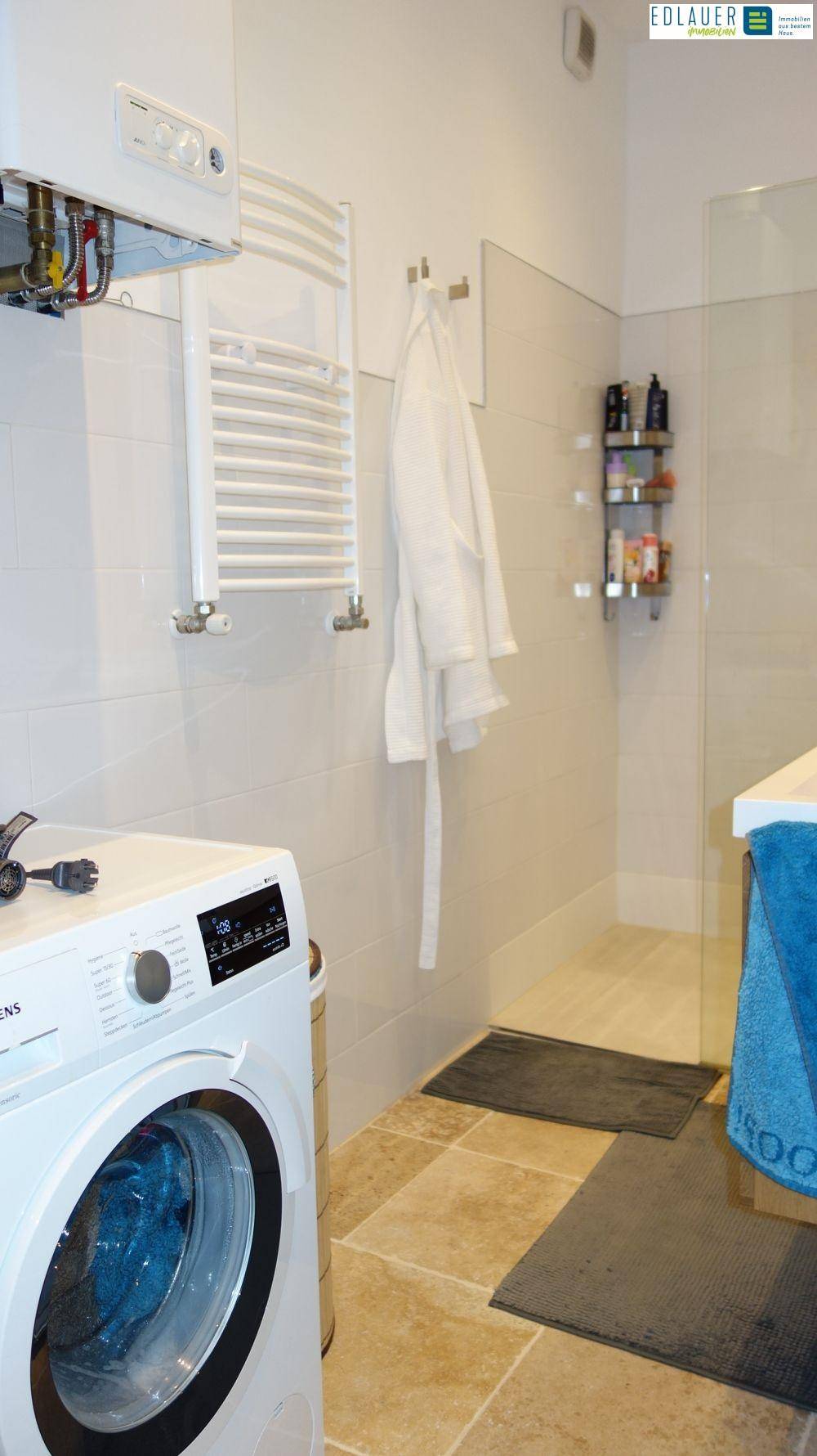 Badezimmer mit Waschmaschine, beheiztem Handtuchhalter und Dusche.