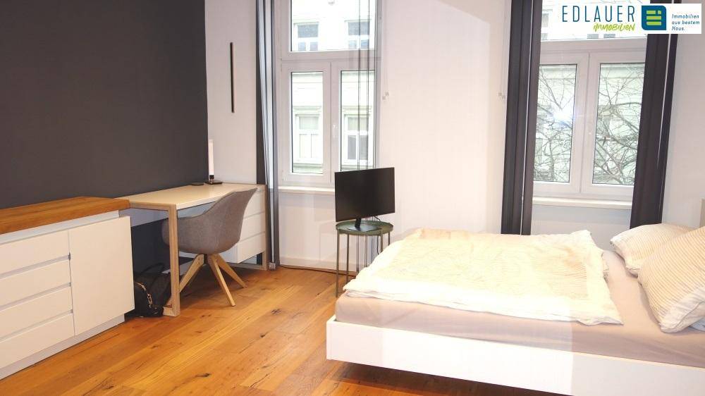 Helles Schlafzimmer mit Holzboden, Schreibtisch und großen Fenstern.