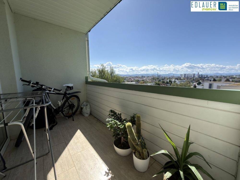 Sonniger Balkon mit Stadtblick und Platz für Pflanzen und Fahrräder.