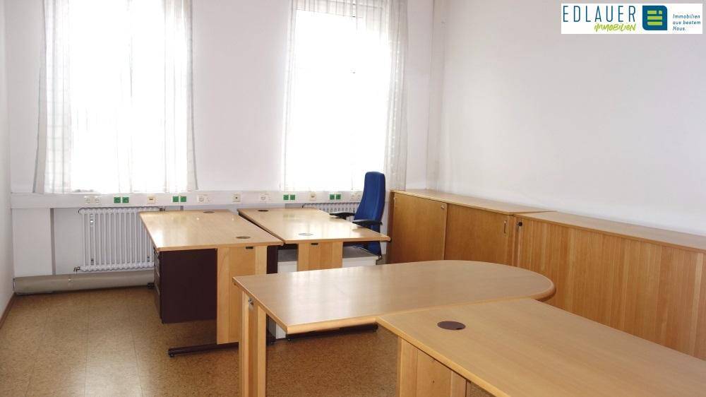 Geräumiges Büro mit mehreren Holzschreibtischen und langen Holzschränken entlang der Wand, hell durch Fenster.