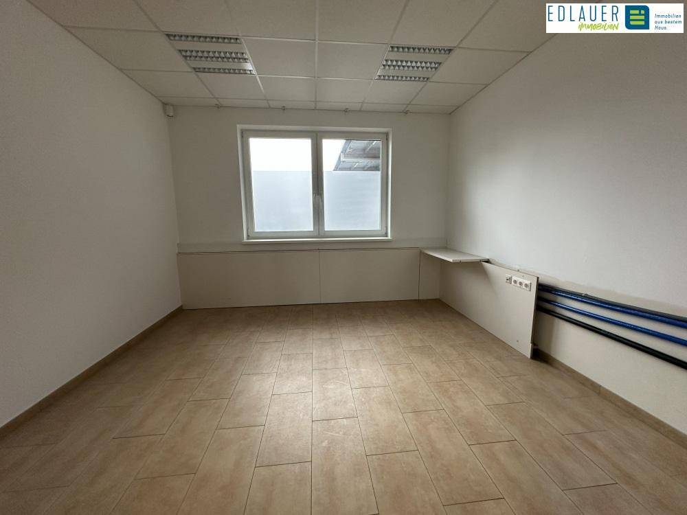 Funktionaler Büroraum mit Fliesenboden, Fenster und sichtbaren Installationen, bietet praktische Arbeitsumgebung.
