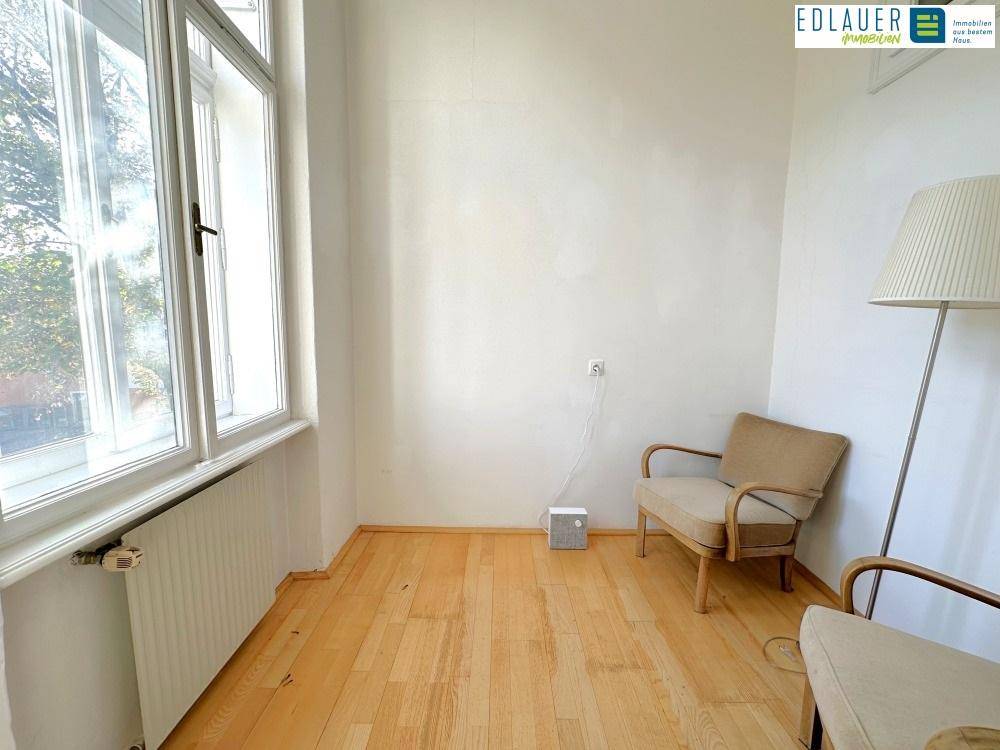 Gemütlicher Raum mit Holzboden, großem Fenster und einem Sessel, ideal als Leseecke oder Wartebereich.