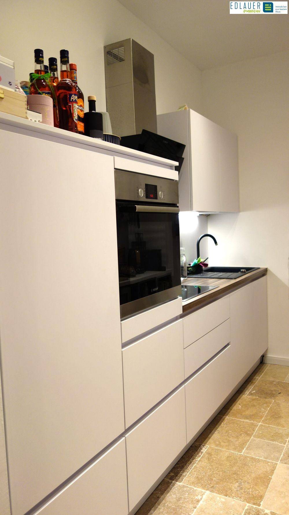 Moderne Küche mit weißen Schränken, Einbauofen und gefliestem Boden.