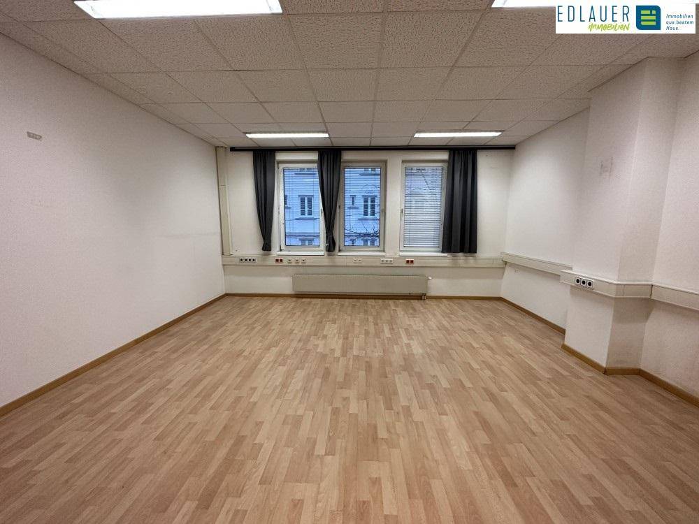 Geräumiger Büroraum mit Laminatboden und Fensterfront, ausgestattet mit Deckenleuchten und Wandsteckdosen.