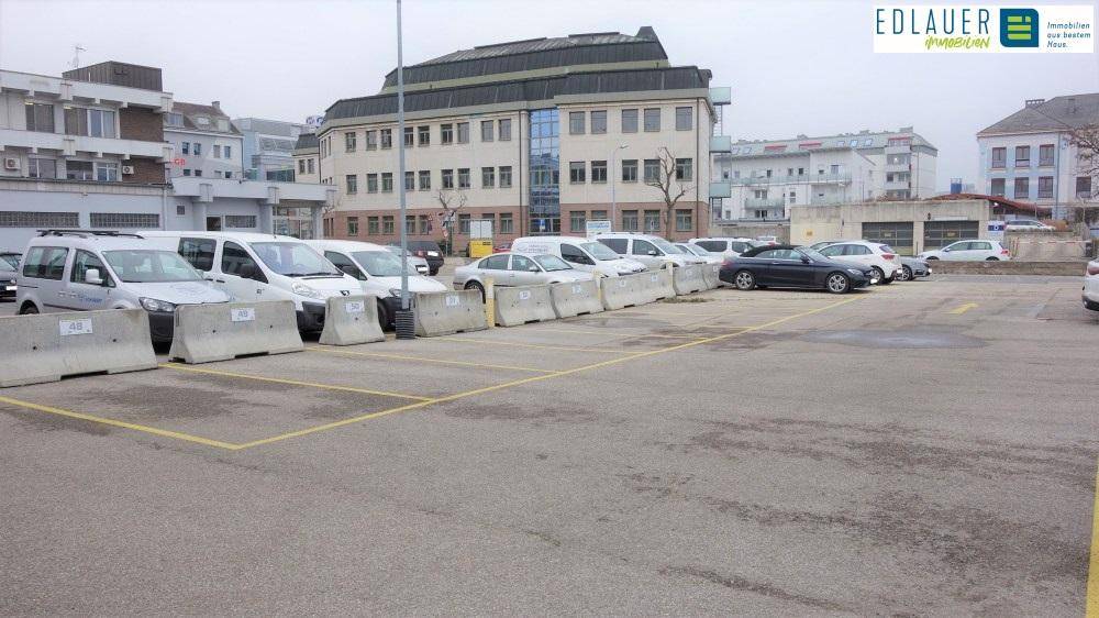 Großer Parkplatz mit geparkten Autos und einem Bürogebäude im Hintergrund.