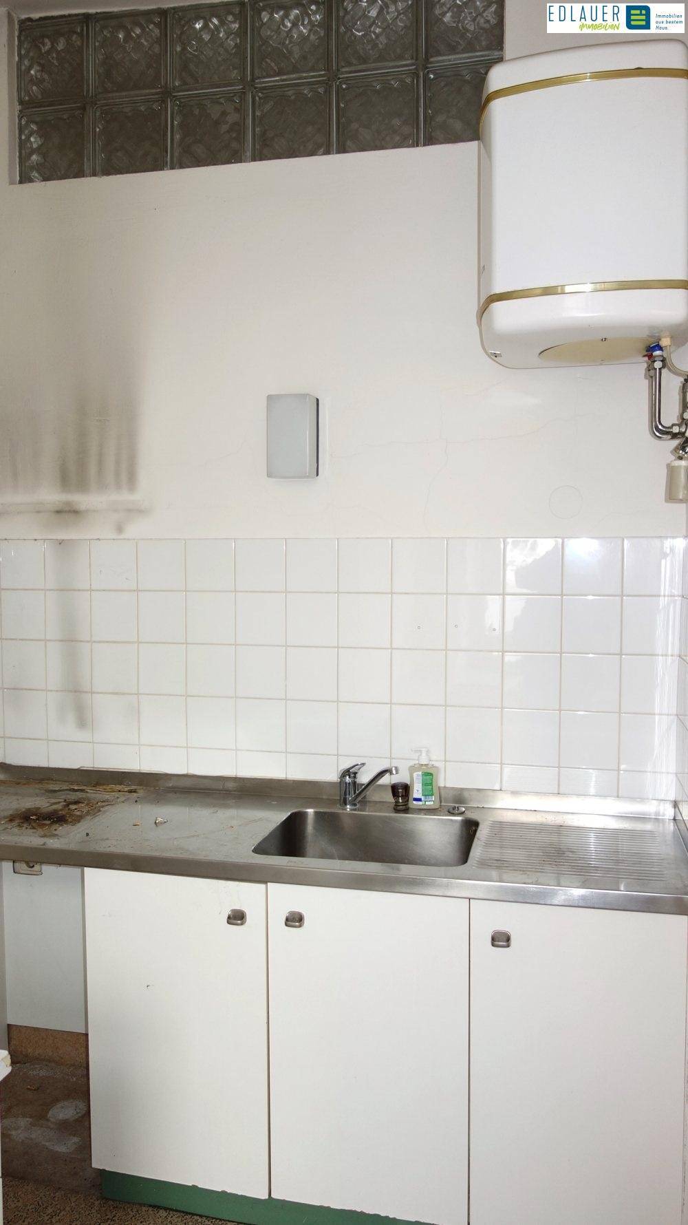 Kleine Küchenzeile mit Spülbecken, weißen Fliesen und einem Warmwasserboiler.