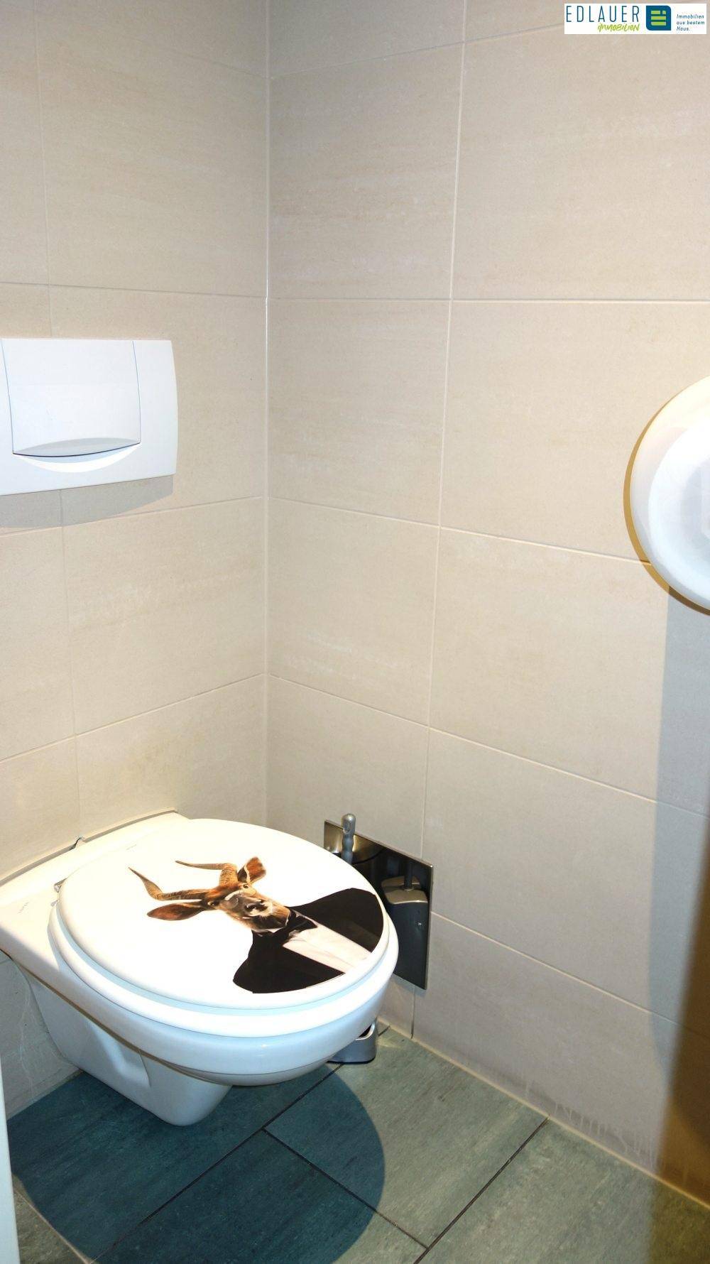 Toilette mit hellgrauen Fliesen und einer wandmontierten Toilette mit einem dekorativen Deckel in einem modernen Stil.