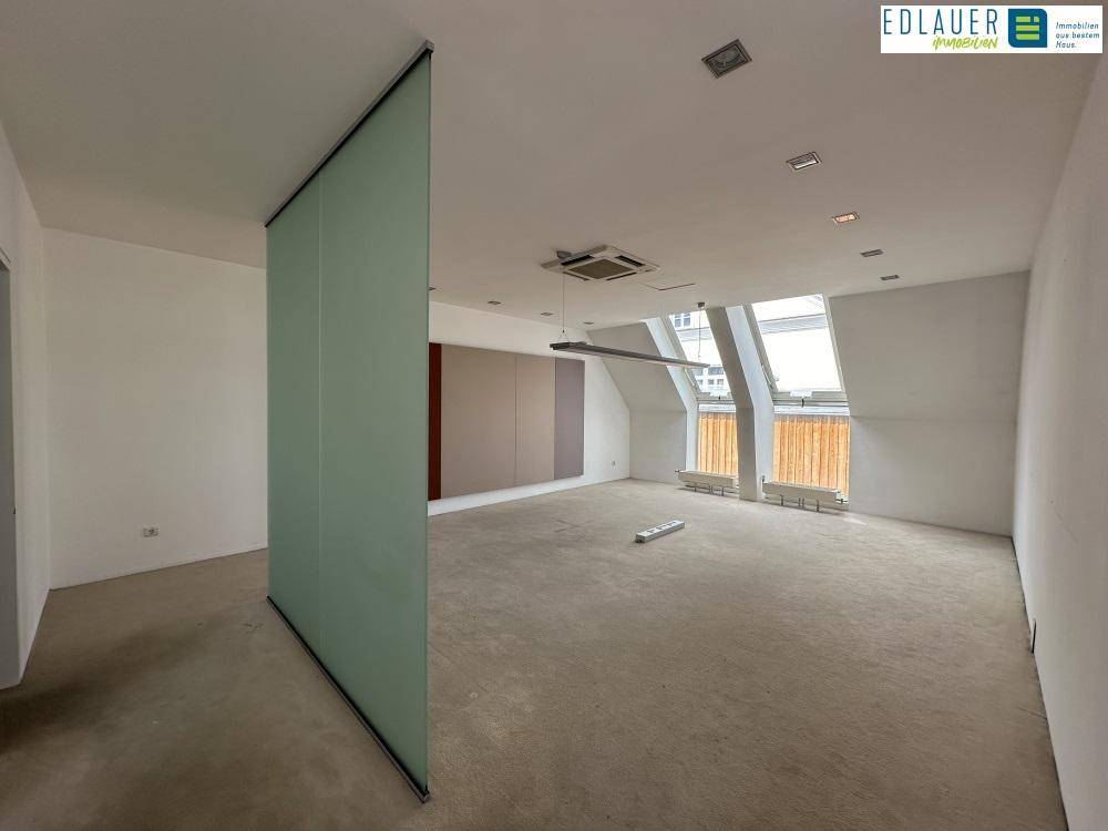 Heller Büroraum im Dachgeschoss mit großen Dachfenstern, schrägen Wänden und einem modernen Glas-Trennelement.