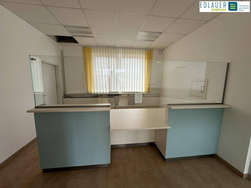 Empfangsbereich mit moderner Theke, Glasschutz und Fenster mit Jalousien, bereit für Kundenempfang.