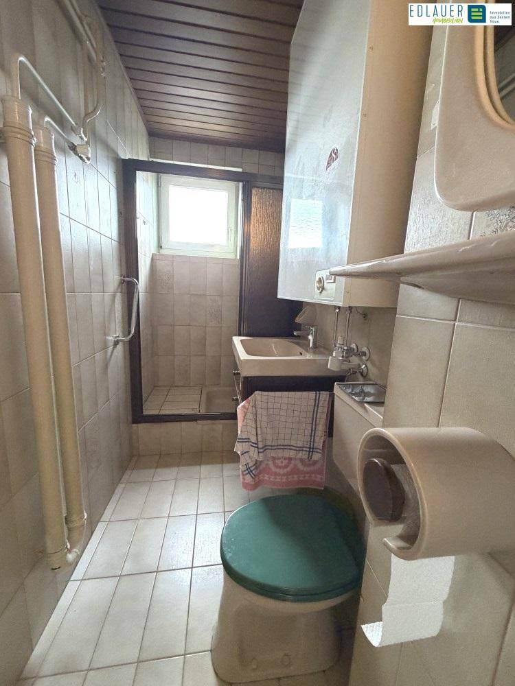 Kleines Badezimmer mit Dusche, WC und Waschbecken, ausgestattet mit Wandfliesen und Holzdecke.
