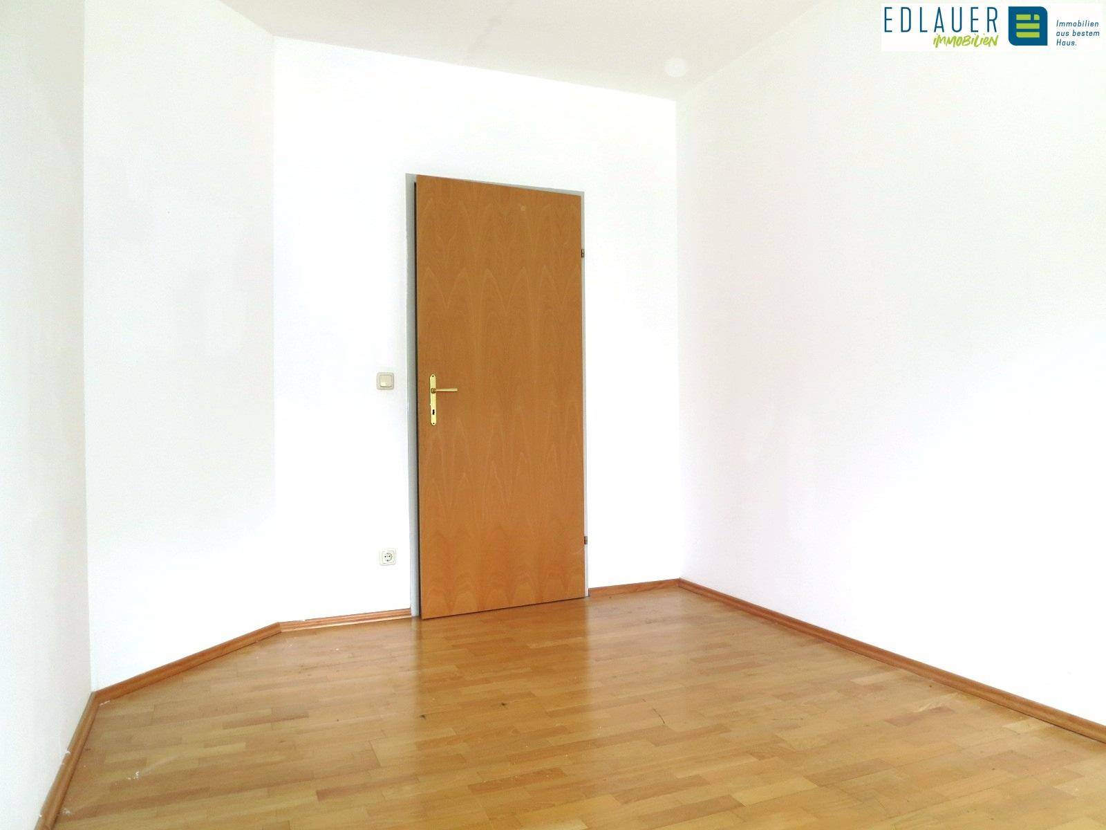 Leeres Zimmer mit Holztür und Parkettboden, ideal für ein gemütliches Schlafzimmer.