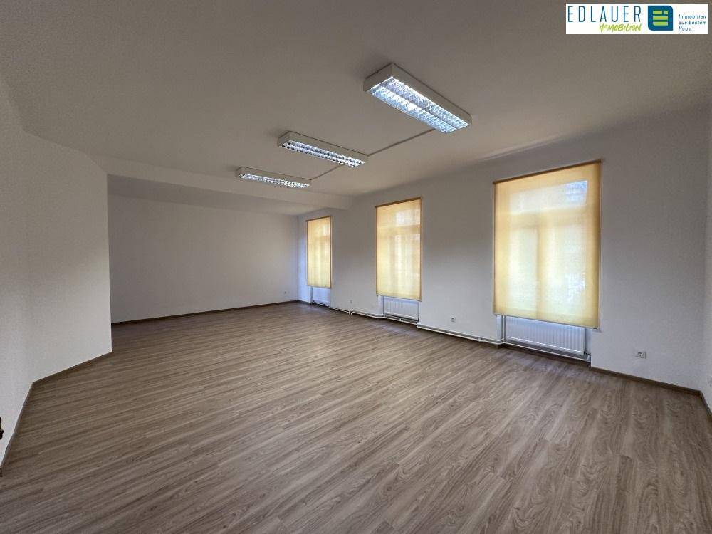 Geräumiger Gewerberaum mit Laminatboden, großen Fenstern und Deckenbeleuchtung, ideal für Büros oder Praxen.