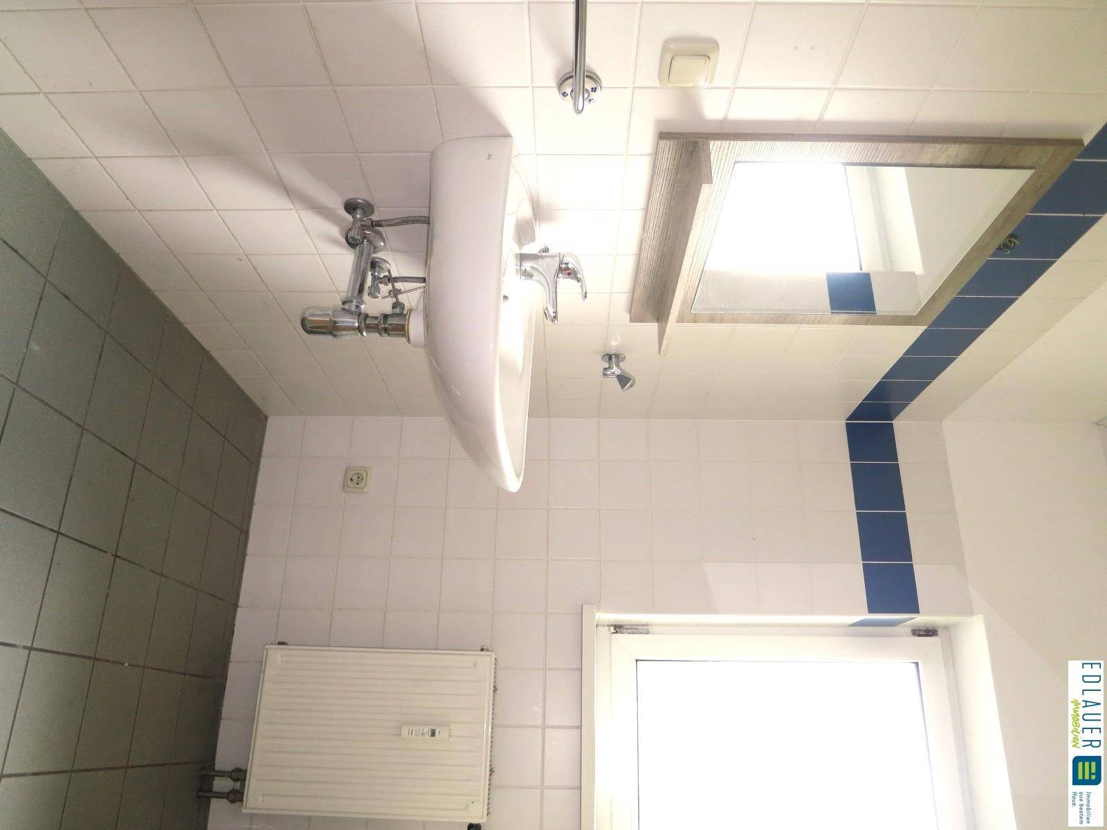 Badezimmer mit Waschbecken, Spiegel und weißen Fliesen, inklusive Fenster für Tageslicht.