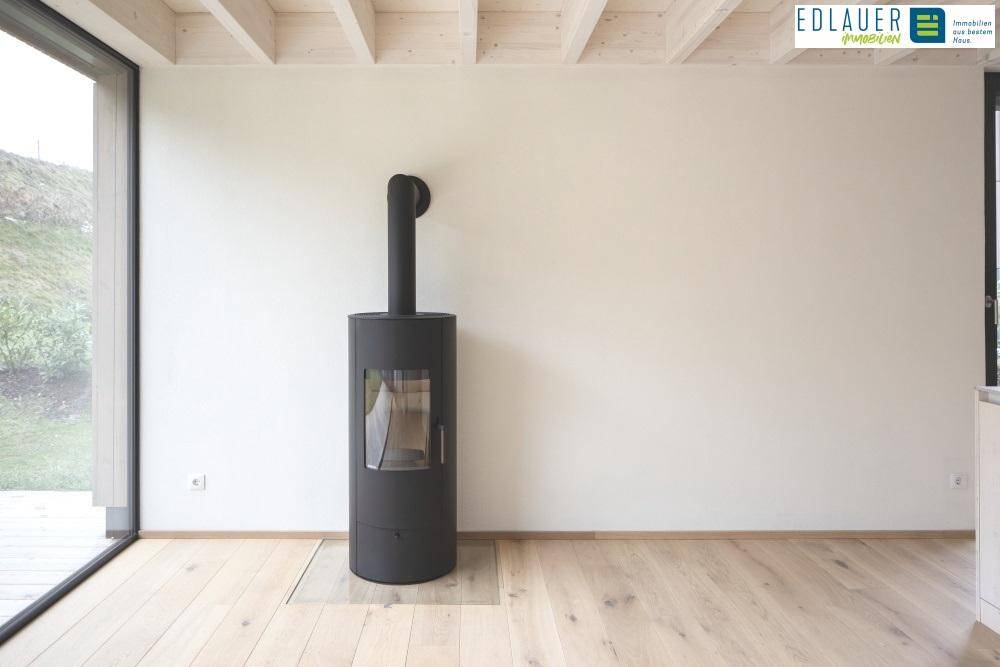 Heller Wohnbereich mit modernem Holzofen und großen Fenstern zum Garten.