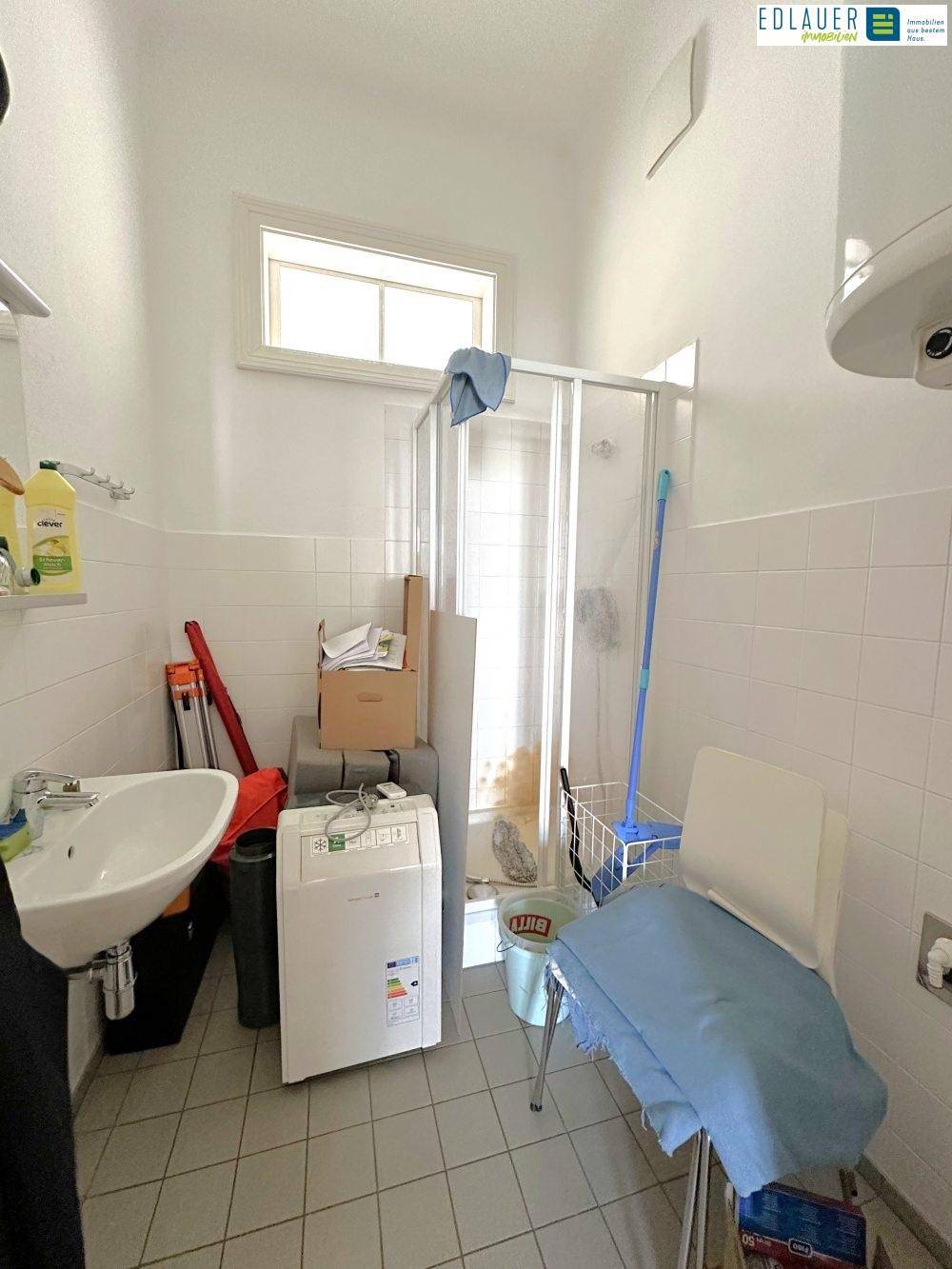 Einfaches Badezimmer mit Duschkabine, Waschbecken und Fliesen, das auch als Waschküche dient.