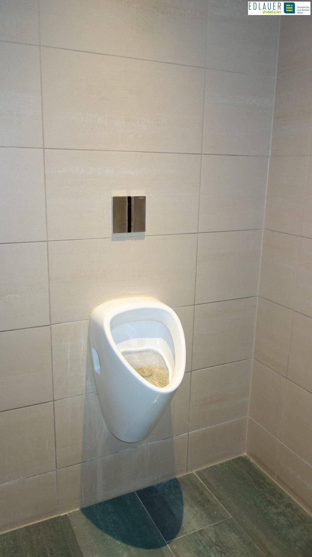Badezimmer mit hellgrauen Fliesen und einem modernen Urinal an der Wand, das eine saubere Ästhetik aufweist.