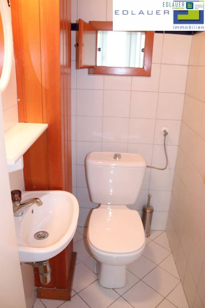 Kleine Gästetoilette mit WC, Handwaschbecken und weißen Fliesen an Wänden und Boden.