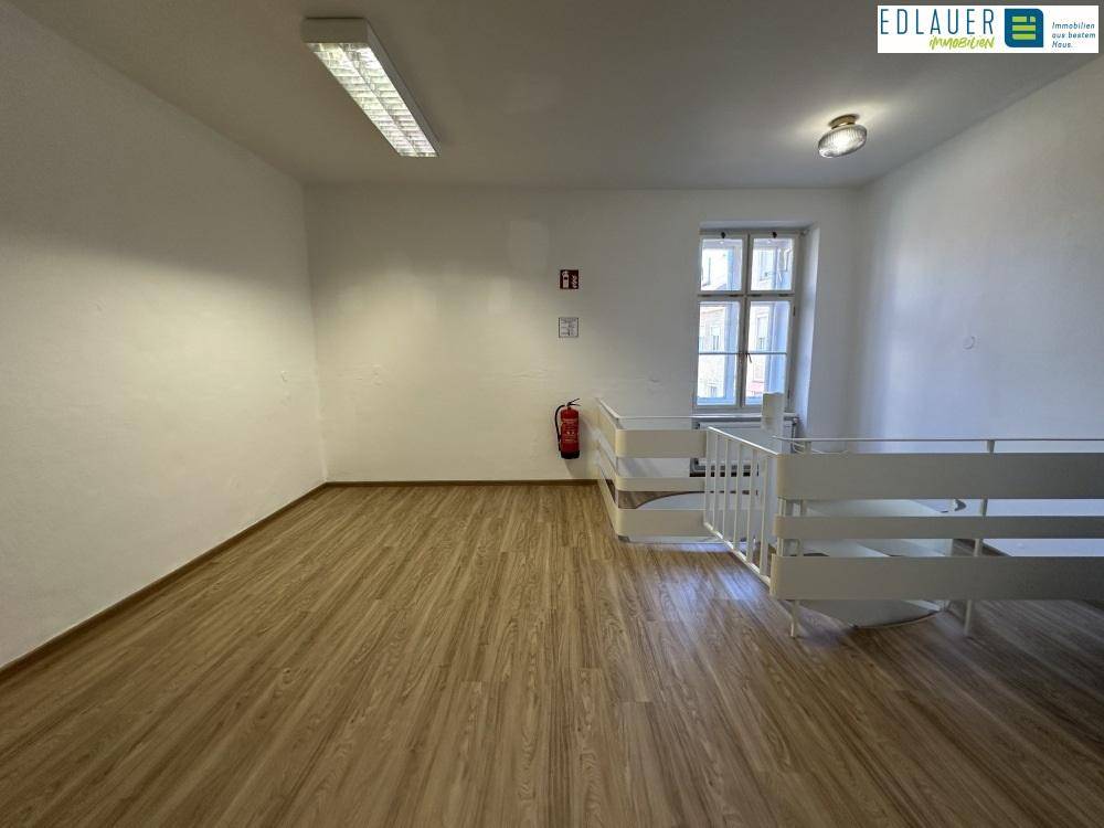 Raum mit Laminatboden, Fenster und Geländer, das einen offenen Bereich abgrenzt.