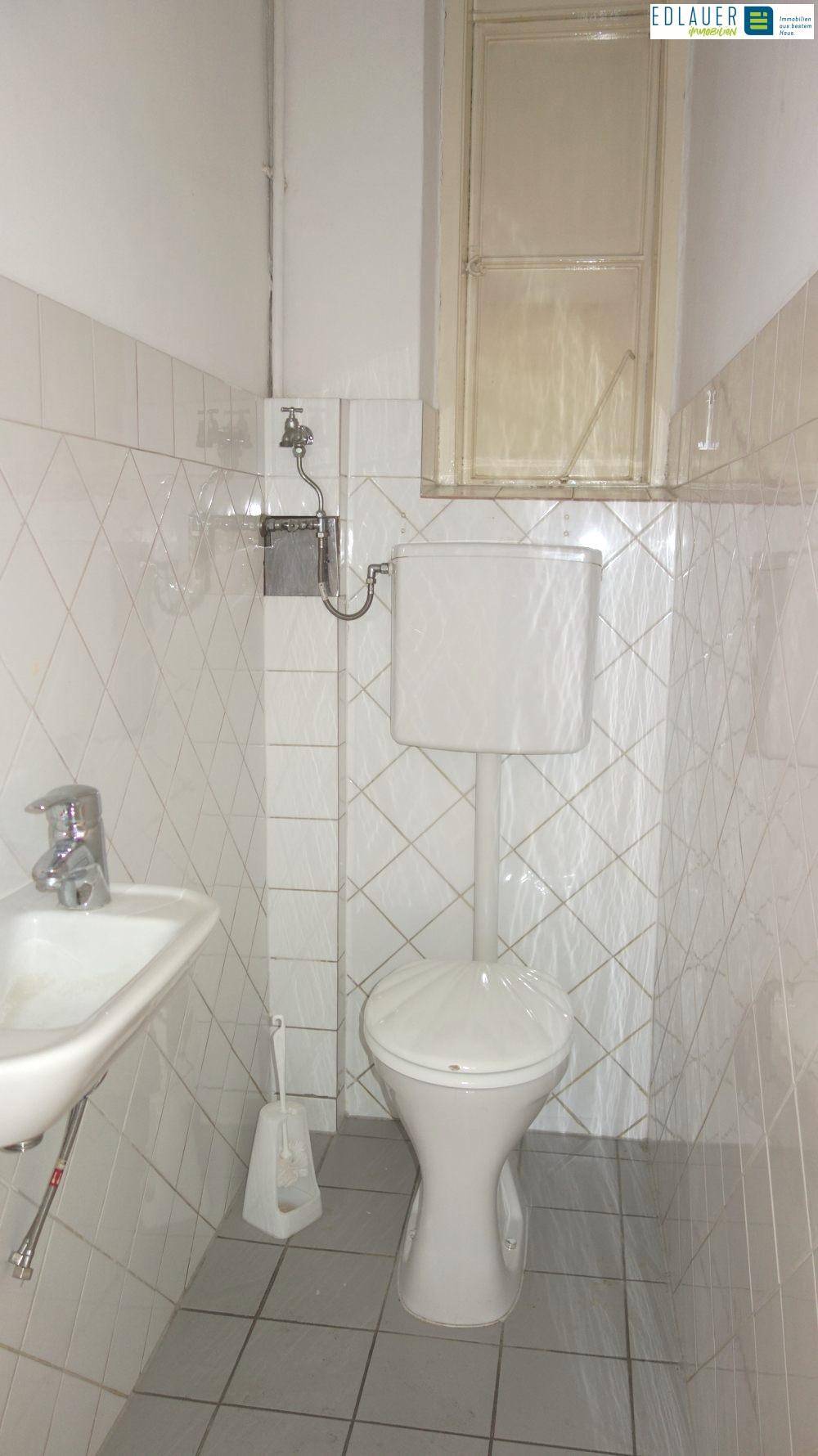 Kleines Badezimmer mit WC, Waschbecken und weißen Fliesen, funktional und einfach gehalten.