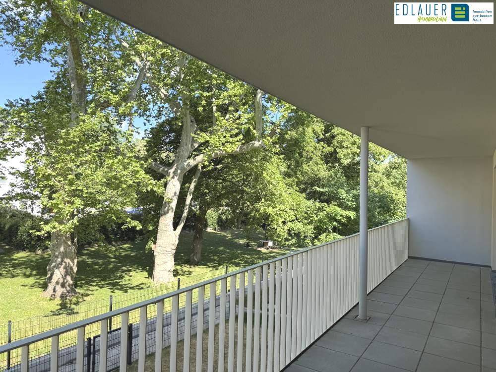 Geräumiger Balkon mit Fliesenboden und einem schönen Blick ins Grüne mit alten Bäumen.