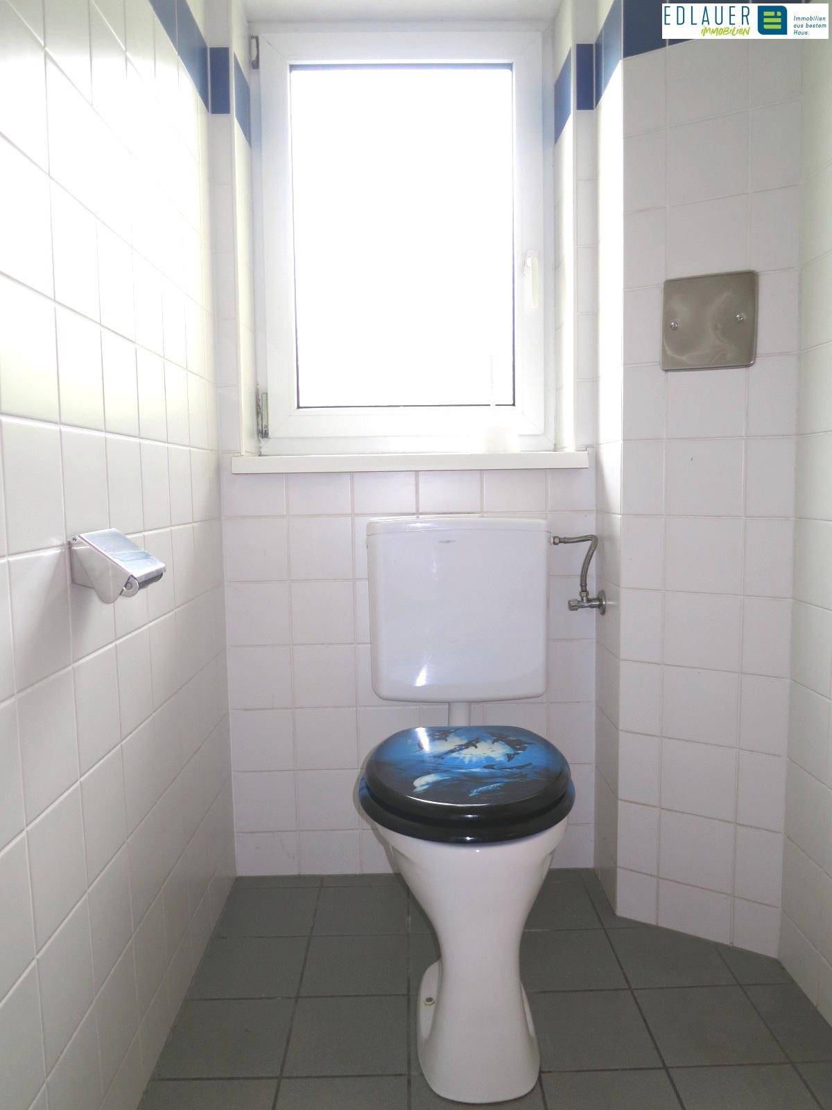 Separates WC mit Fenster, Toilette und weißen Fliesen, praktisch und hell.