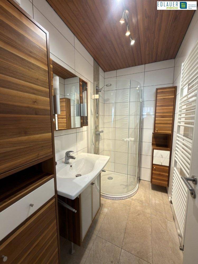 Modernes Badezimmer mit Duschkabine, Waschbecken und Holzmöbeln.