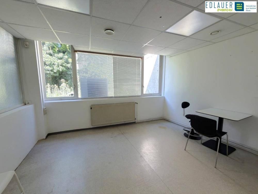 Leeres Büro mit großen Fenstern, Heizkörper und einem kleinen Tisch, bietet viel Tageslicht.