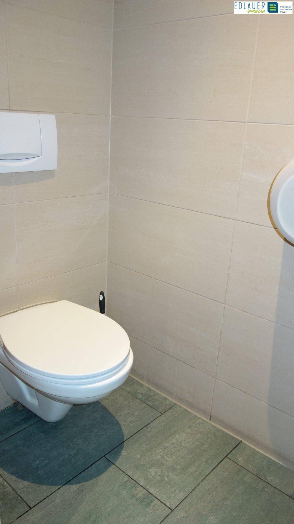 Toilette mit hellgrauen Fliesen und einer wandmontierten Toilette in einem sauberen und funktionalen Raum.